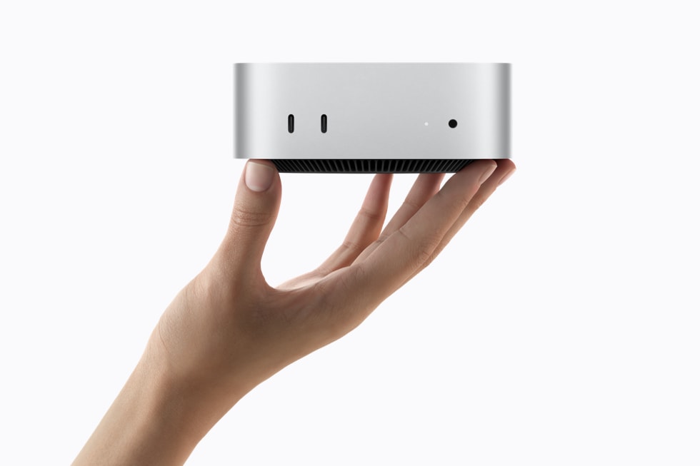 Ruka držící stříbrný Mac mini s porty na přední straně
